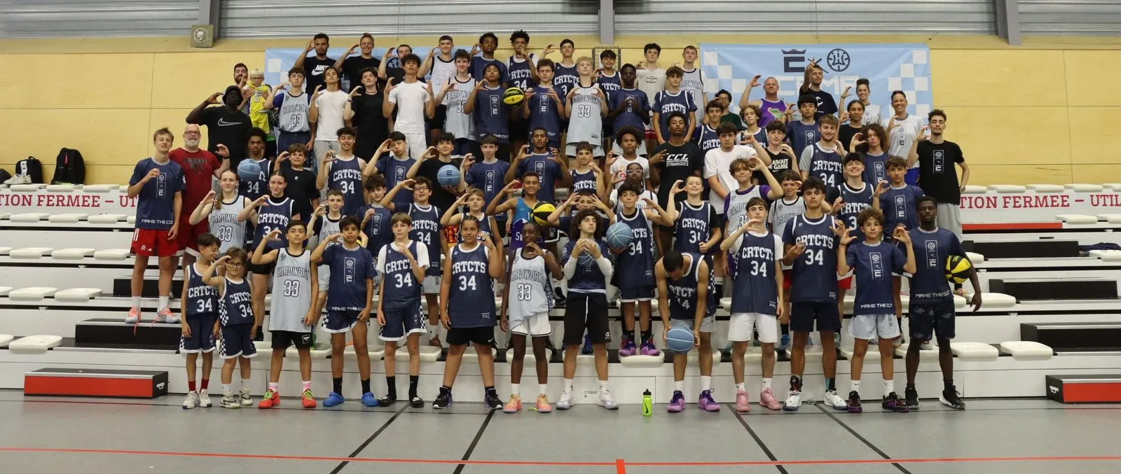 La photo de groupe d'un camp Hardwork × CourtCuts : une soixantaine de joueurs et leurs coachs dans les tribunes du gymnase
