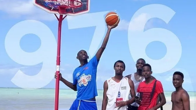 Un joueur lève le ballon vers un panier planté dans le sable, six autres autour de lui, sur une plage de Mayotte